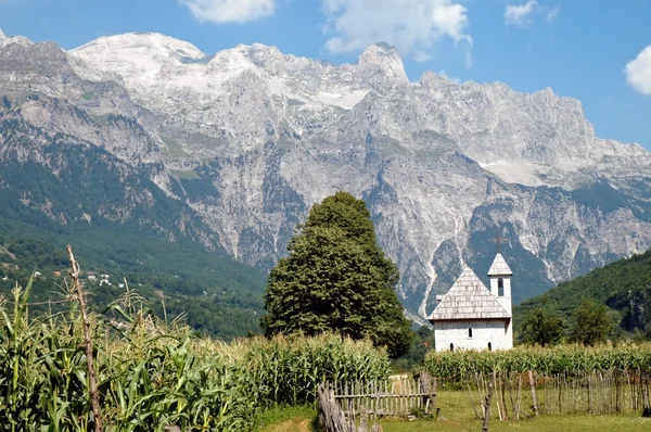 Sprachporträt Albanisch: Kirche in Theth vor der Kulisse der Albanischen Alpen